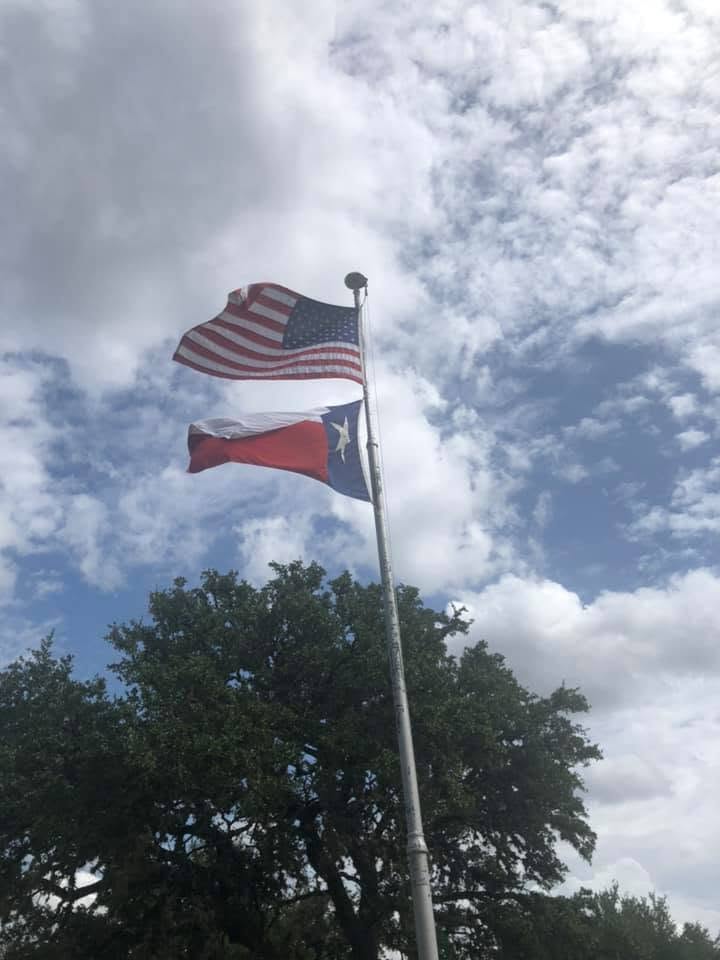 The United States and Texas flags flying from the flagpole in the Casparis section, live oaks below.